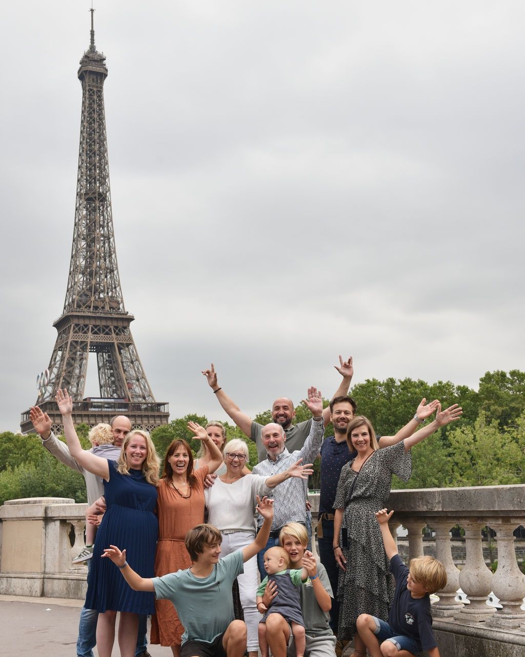 Une famille de trois générations lève les bras devant la tour Eiffel.